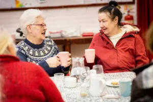 Two women smiling and chatting over cups of tea at a group session