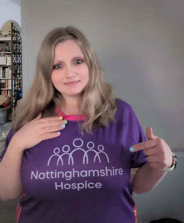 A woman wearing a purple Nottinghamshire Hospice T-shirt points towards the hospice logo.