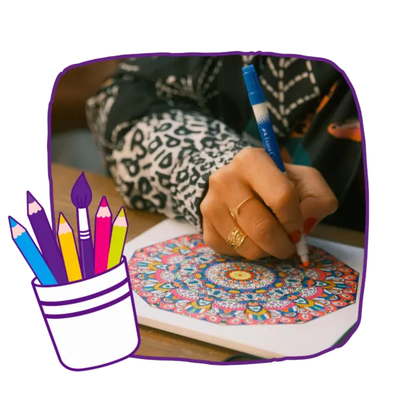 A person colouring an intricate circular pattern with felt-tip pens at a wooden table.