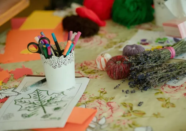 Craft materials on a table, including pens, scissors, paper, wool decorations and dried lavender.